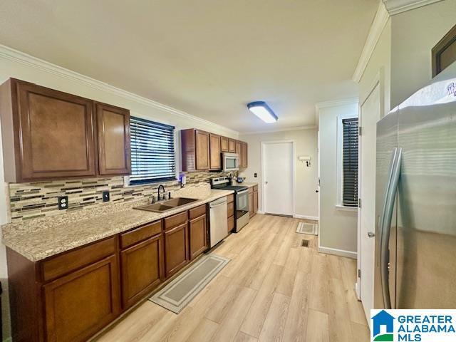 kitchen featuring ornamental molding, stainless steel appliances, decorative backsplash, a sink, and light wood finished floors