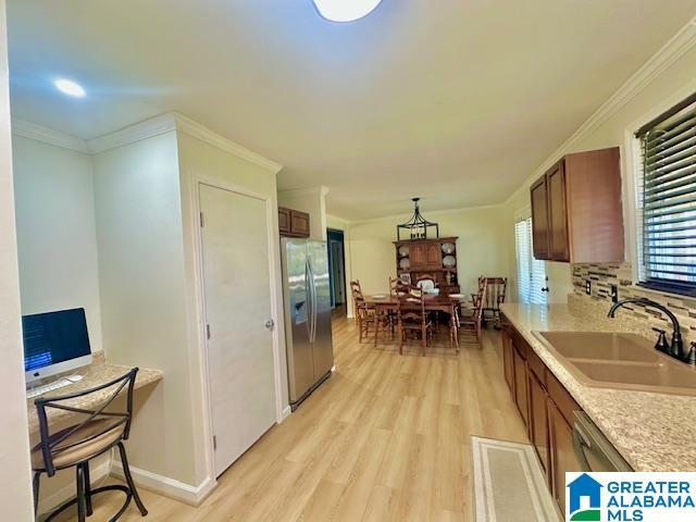 kitchen with light countertops, stainless steel refrigerator with ice dispenser, crown molding, a sink, and brown cabinets