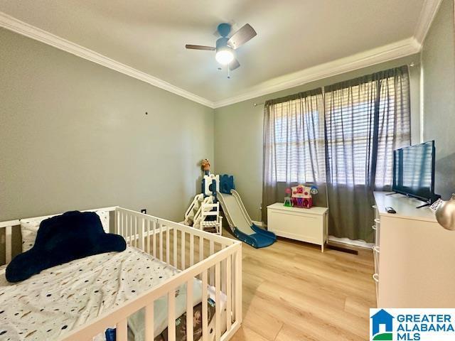 bedroom featuring light wood-style floors, a crib, ornamental molding, and a ceiling fan