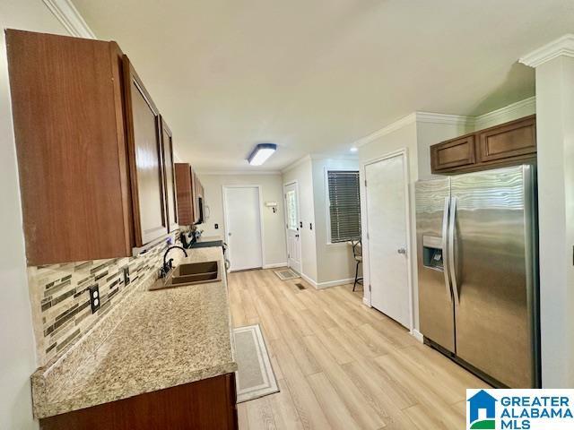 kitchen with stainless steel refrigerator with ice dispenser, ornamental molding, backsplash, a sink, and light wood finished floors