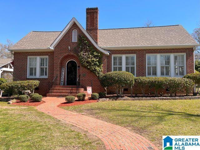 tudor house with a chimney, brick siding, a shingled roof, and a front lawn