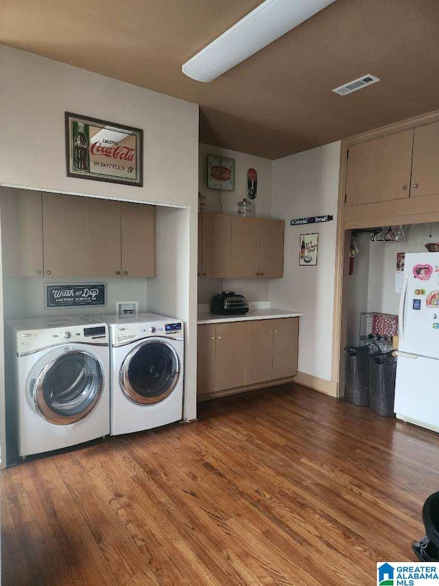 washroom with washing machine and clothes dryer, cabinet space, wood finished floors, and visible vents