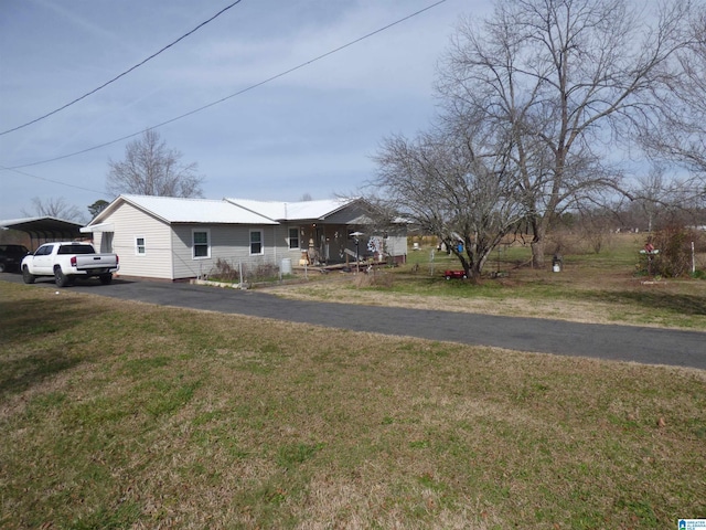 view of front facade featuring driveway, metal roof, a front lawn, and a carport