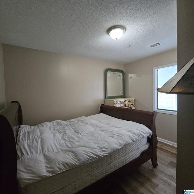 bedroom featuring a textured ceiling, visible vents, wood finished floors, and baseboards
