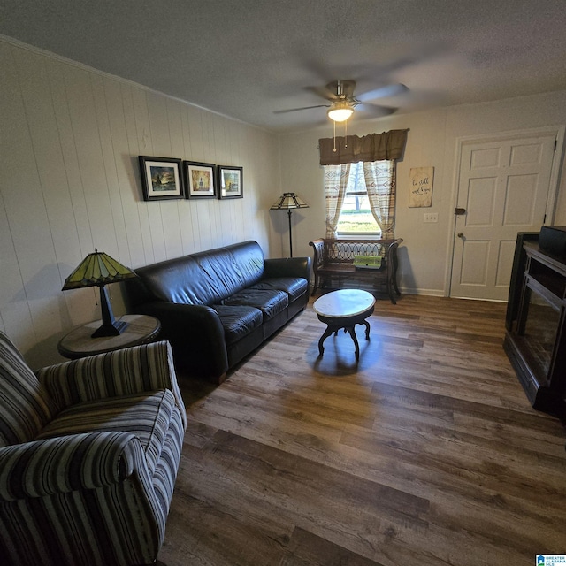 living area featuring a ceiling fan, baseboards, wood finished floors, and a textured ceiling
