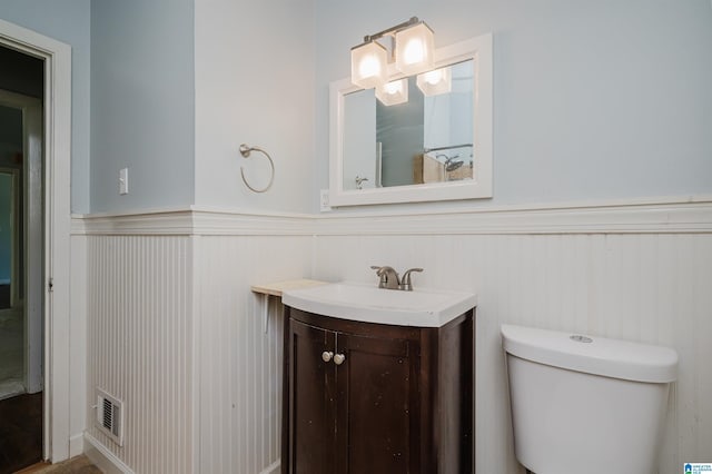 bathroom featuring toilet, vanity, wainscoting, and visible vents