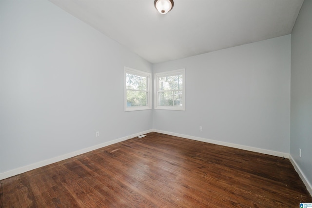 spare room featuring dark wood-style floors, baseboards, and vaulted ceiling