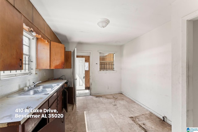 kitchen with baseboards, light countertops, a sink, and brown cabinetry