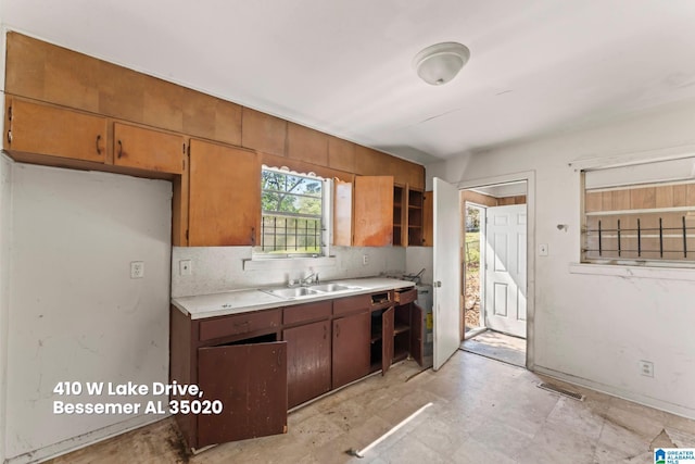 kitchen with light countertops, tasteful backsplash, a sink, visible vents, and brown cabinetry