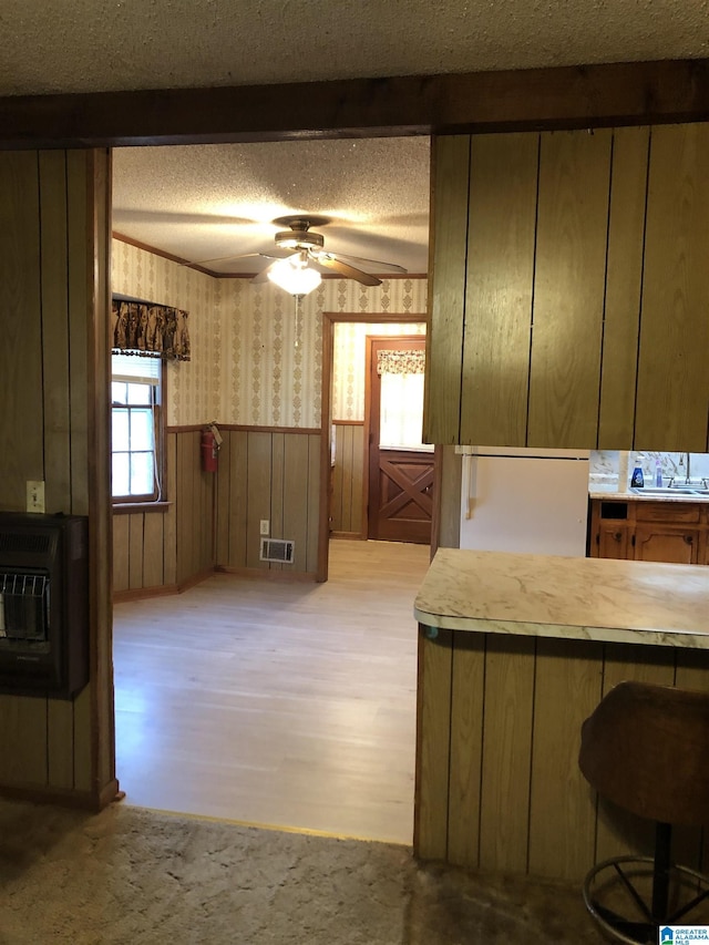 kitchen featuring heating unit, a ceiling fan, a textured ceiling, visible vents, and wallpapered walls