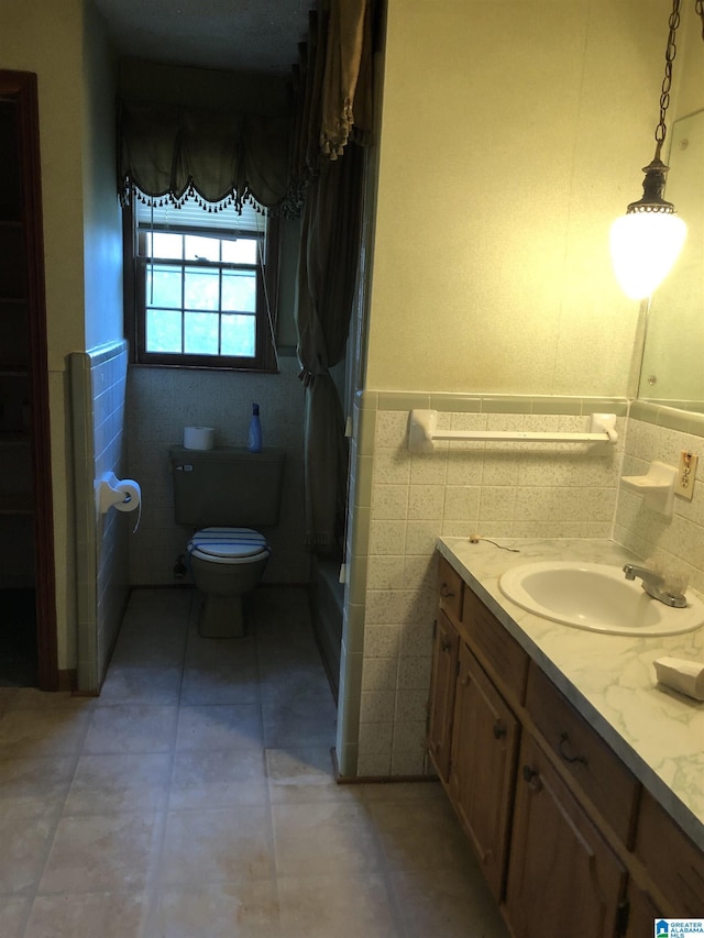 bathroom featuring tile walls, toilet, tile patterned floors, vanity, and wainscoting