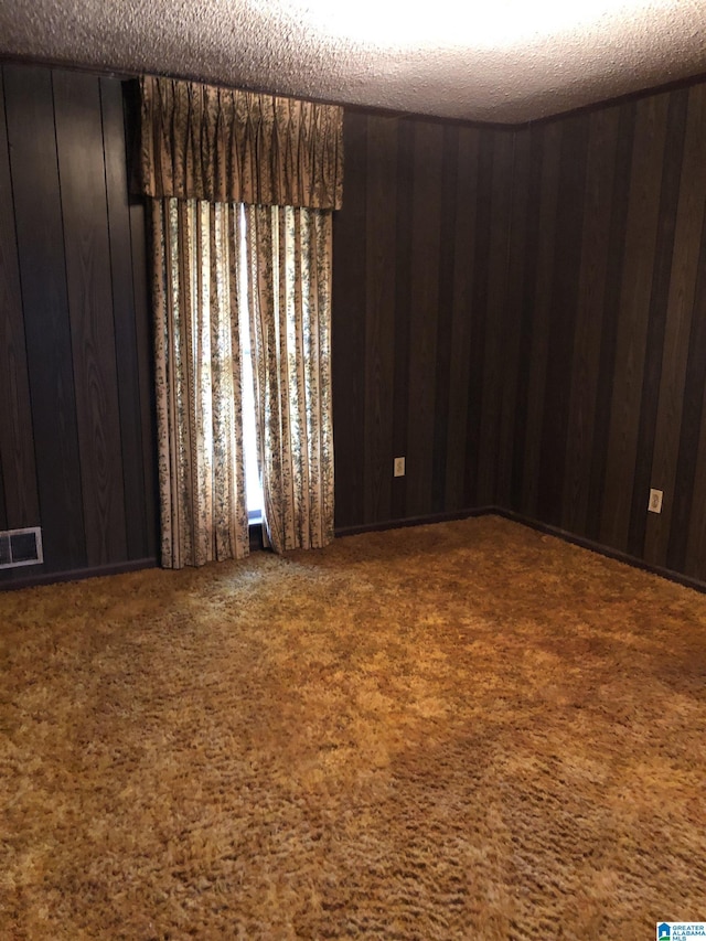 carpeted empty room featuring visible vents, a textured ceiling, and wood walls