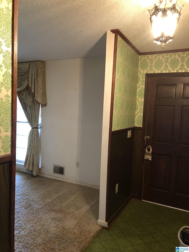 foyer with wallpapered walls, visible vents, a textured ceiling, and wainscoting