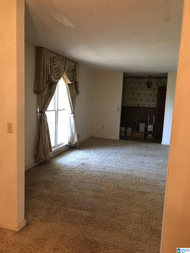 unfurnished living room with wallpapered walls, carpet floors, baseboards, and a textured ceiling