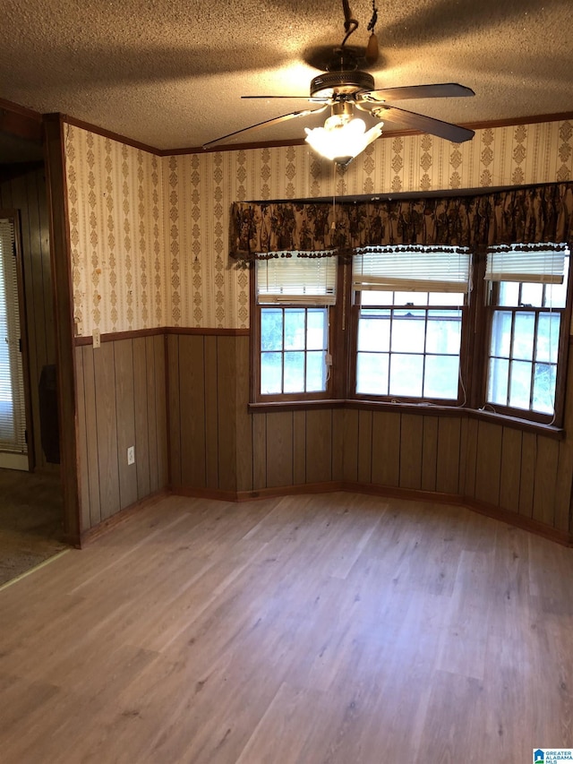 spare room with a wainscoted wall, wallpapered walls, light wood-style floors, and a textured ceiling