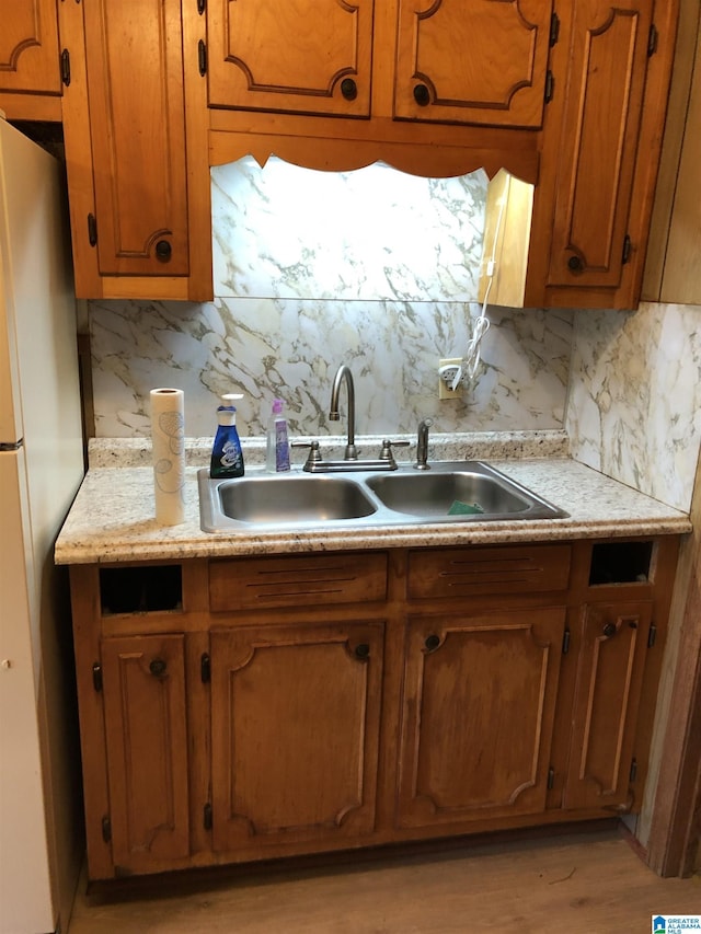 kitchen with light countertops, a sink, brown cabinetry, and freestanding refrigerator