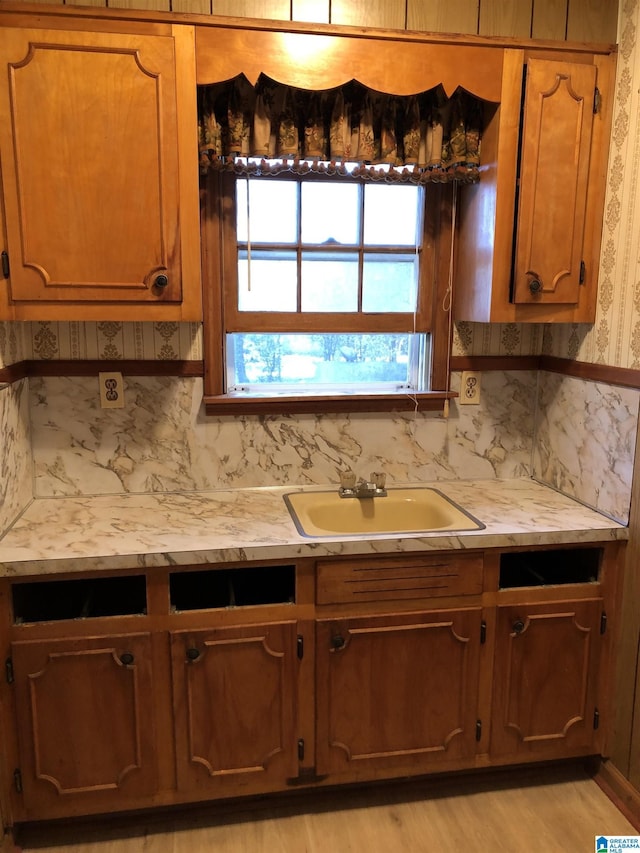 kitchen with light countertops, brown cabinets, tasteful backsplash, a sink, and light wood-style floors