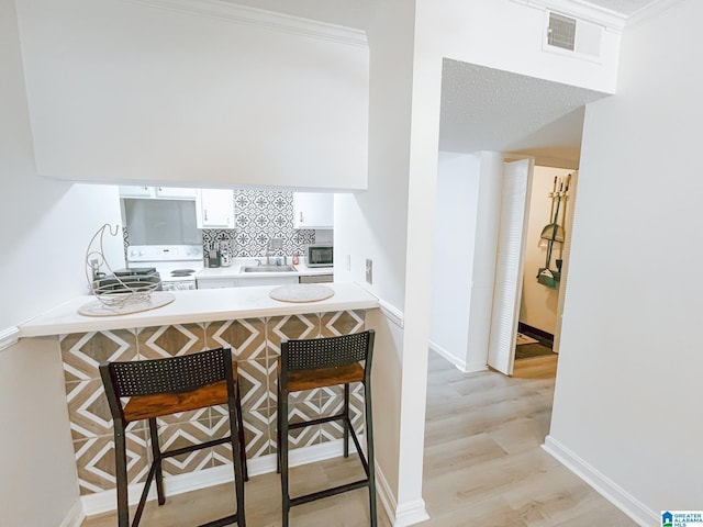 kitchen featuring white cabinets, visible vents, a kitchen bar, a sink, and electric range
