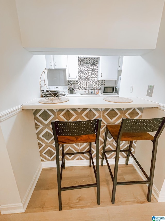 kitchen featuring white cabinetry, light countertops, a breakfast bar area, stainless steel microwave, and a sink