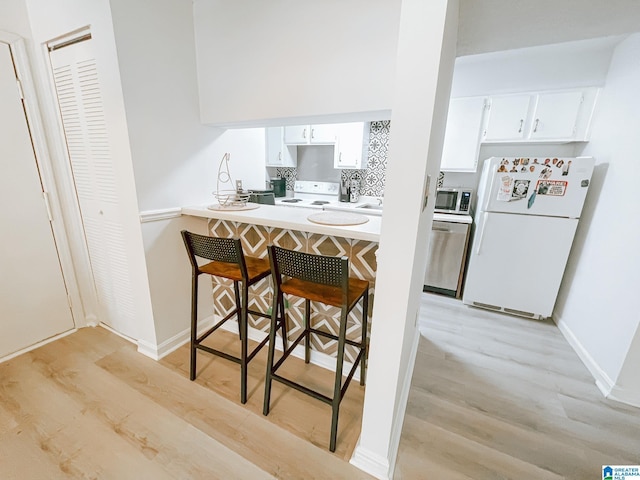 kitchen featuring white cabinets, a kitchen bar, light wood-style floors, and appliances with stainless steel finishes