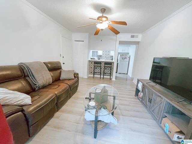 living area with a textured ceiling, ornamental molding, visible vents, and a ceiling fan