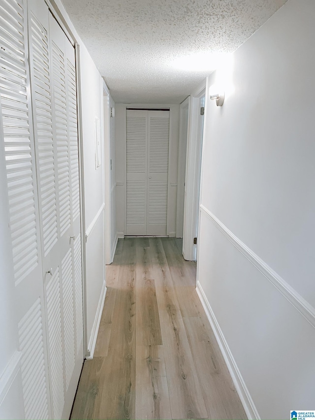 corridor featuring baseboards, a textured ceiling, and light wood-style floors