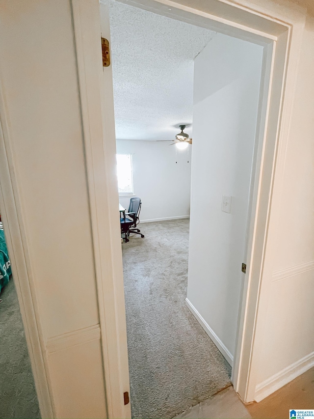 hall featuring baseboards, carpet flooring, and a textured ceiling