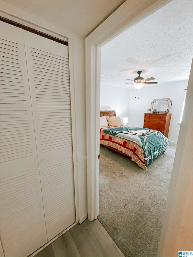 bedroom with carpet flooring, a textured ceiling, ceiling fan, a closet, and wood finished floors