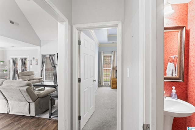 corridor with visible vents, dark wood-style flooring, ornamental molding, vaulted ceiling, and wallpapered walls
