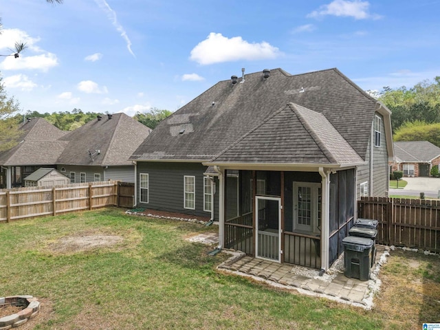 rear view of property featuring a shingled roof, a fenced backyard, a sunroom, and a lawn