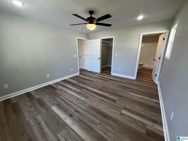 unfurnished bedroom with dark wood-type flooring, connected bathroom, baseboards, and ceiling fan