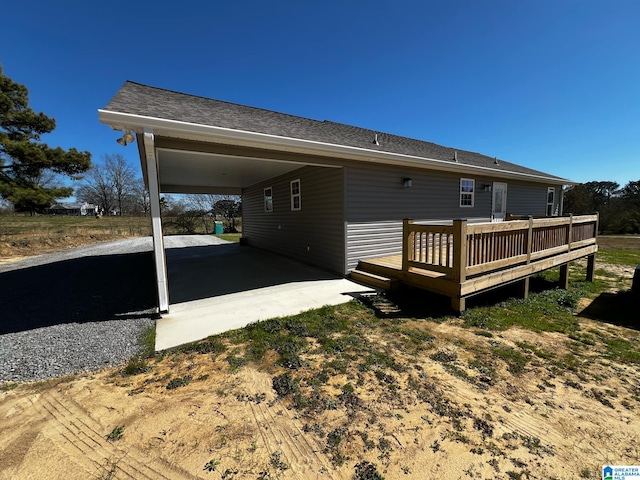 back of house with driveway, a deck, and a carport