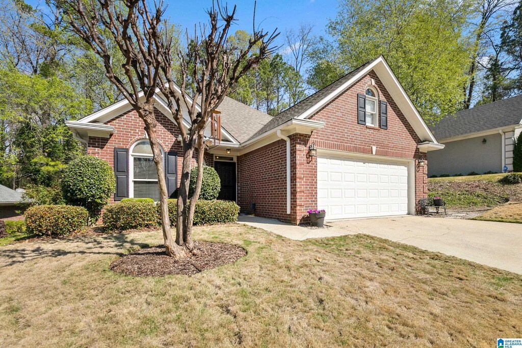 view of front of property with a front lawn, roof with shingles, brick siding, and concrete driveway