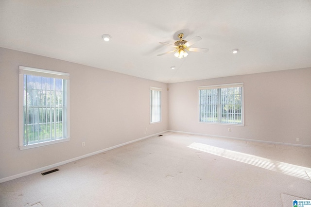 spare room featuring light colored carpet, visible vents, baseboards, and a ceiling fan