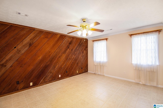 unfurnished room featuring a ceiling fan, ornamental molding, wooden walls, and visible vents