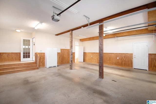 garage featuring a garage door opener, wainscoting, wooden walls, and freestanding refrigerator