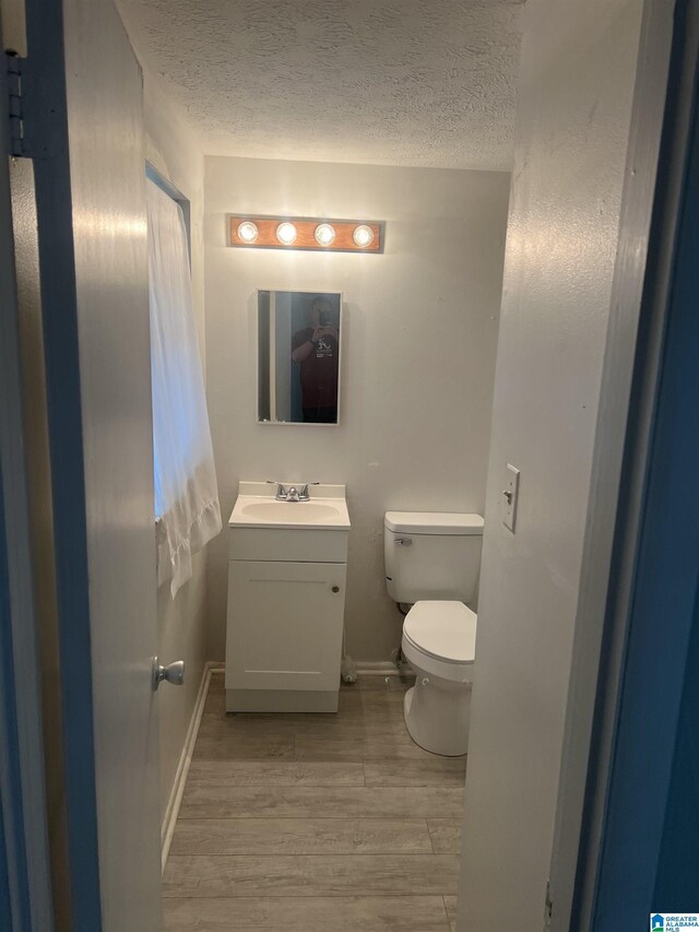 bathroom with toilet, vanity, a textured ceiling, and wood finished floors