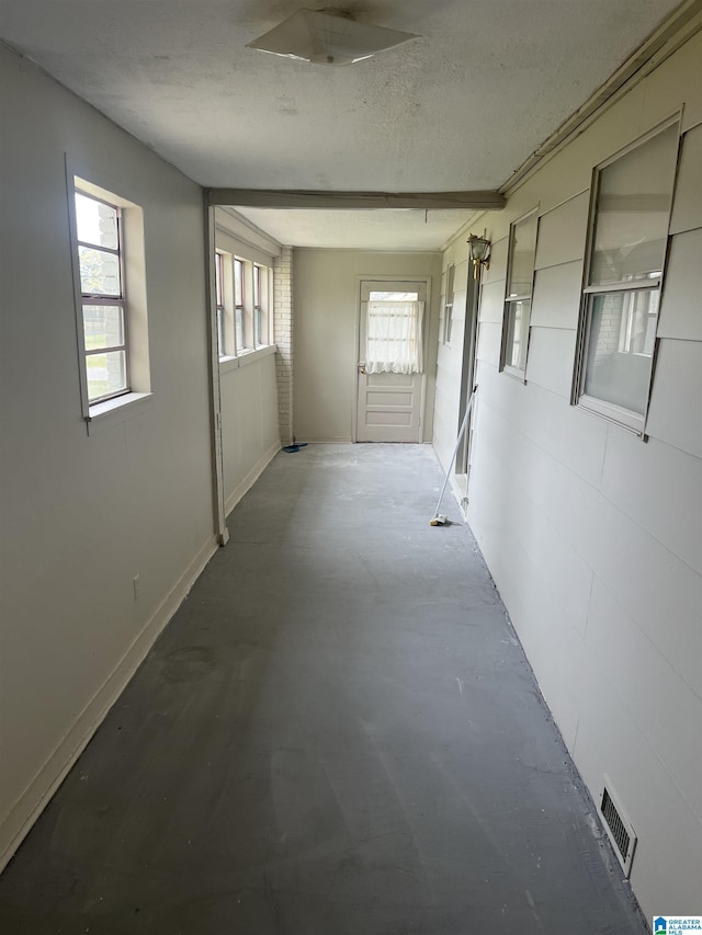 corridor with concrete flooring, a textured ceiling, a healthy amount of sunlight, and visible vents