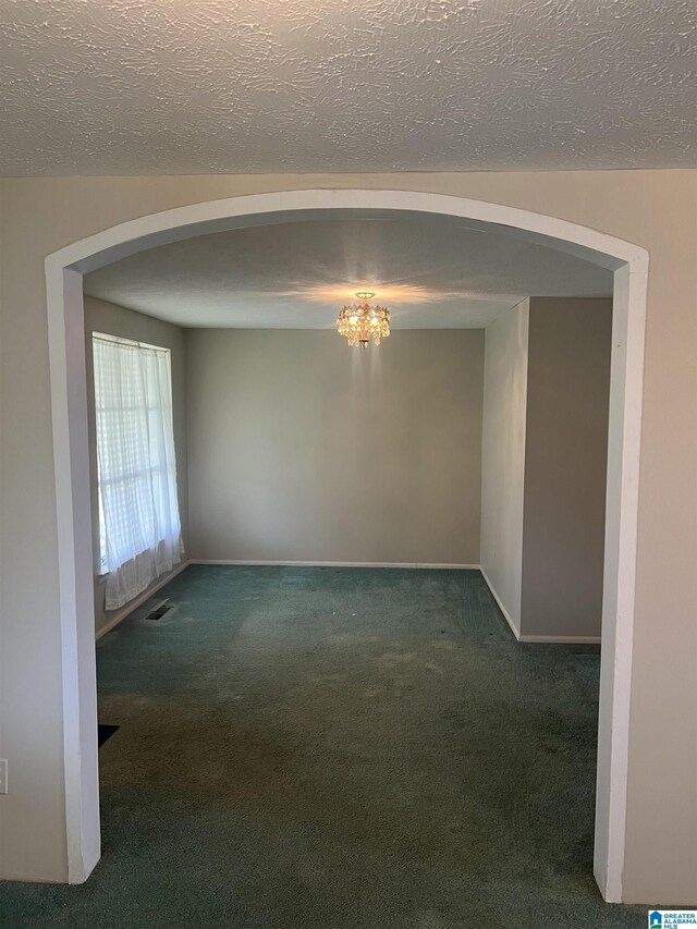 spare room featuring carpet flooring, an inviting chandelier, a textured ceiling, arched walkways, and visible vents