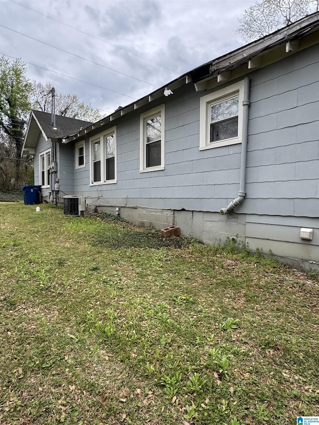 view of side of home with central AC unit, a lawn, and crawl space