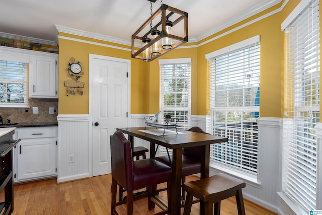 dining area featuring a chandelier, ornamental molding, a wainscoted wall, and light wood-style flooring