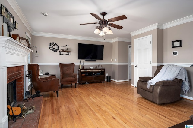 living area featuring baseboards, ceiling fan, a fireplace, crown molding, and light wood-style flooring