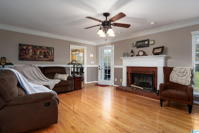 living room featuring light wood finished floors, crown molding, ceiling fan, and a fireplace
