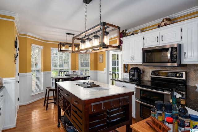 kitchen with appliances with stainless steel finishes, light wood-style floors, crown molding, white cabinetry, and wainscoting