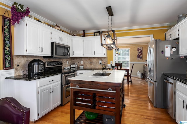 kitchen with white cabinets, crown molding, light wood finished floors, stainless steel appliances, and decorative backsplash