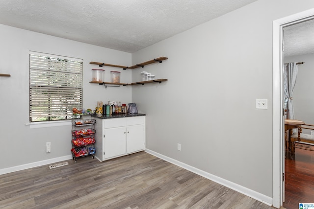bar with a bar, a textured ceiling, baseboards, and wood finished floors