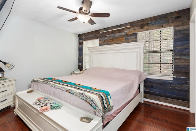 bedroom with a ceiling fan, wooden walls, and dark wood finished floors