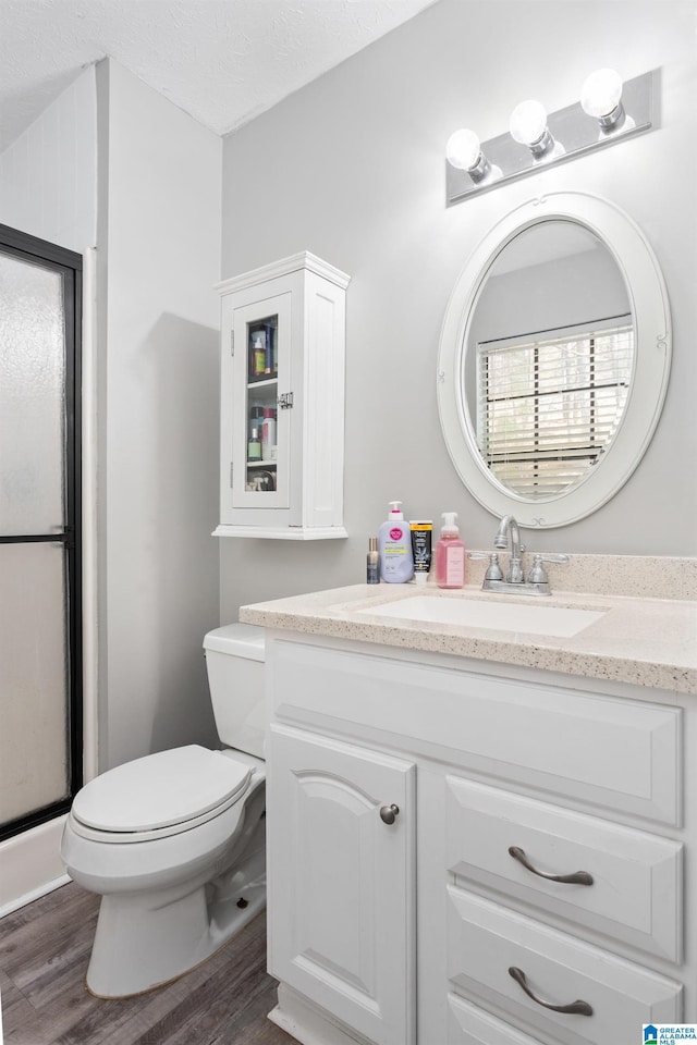 bathroom featuring vanity, toilet, a textured ceiling, a stall shower, and wood finished floors