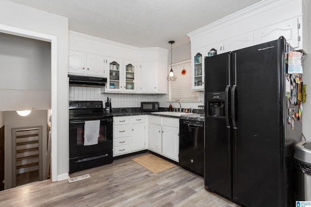 kitchen featuring under cabinet range hood, a sink, dark countertops, white cabinets, and black appliances
