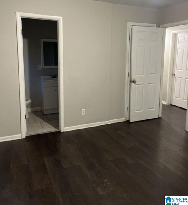 unfurnished bedroom with wood finished floors, baseboards, ensuite bathroom, and a sink